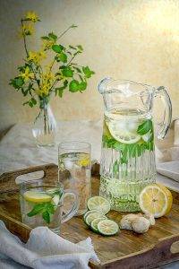 painted picture of a water pitcher with two water glasses filled with water, lemons and limes.